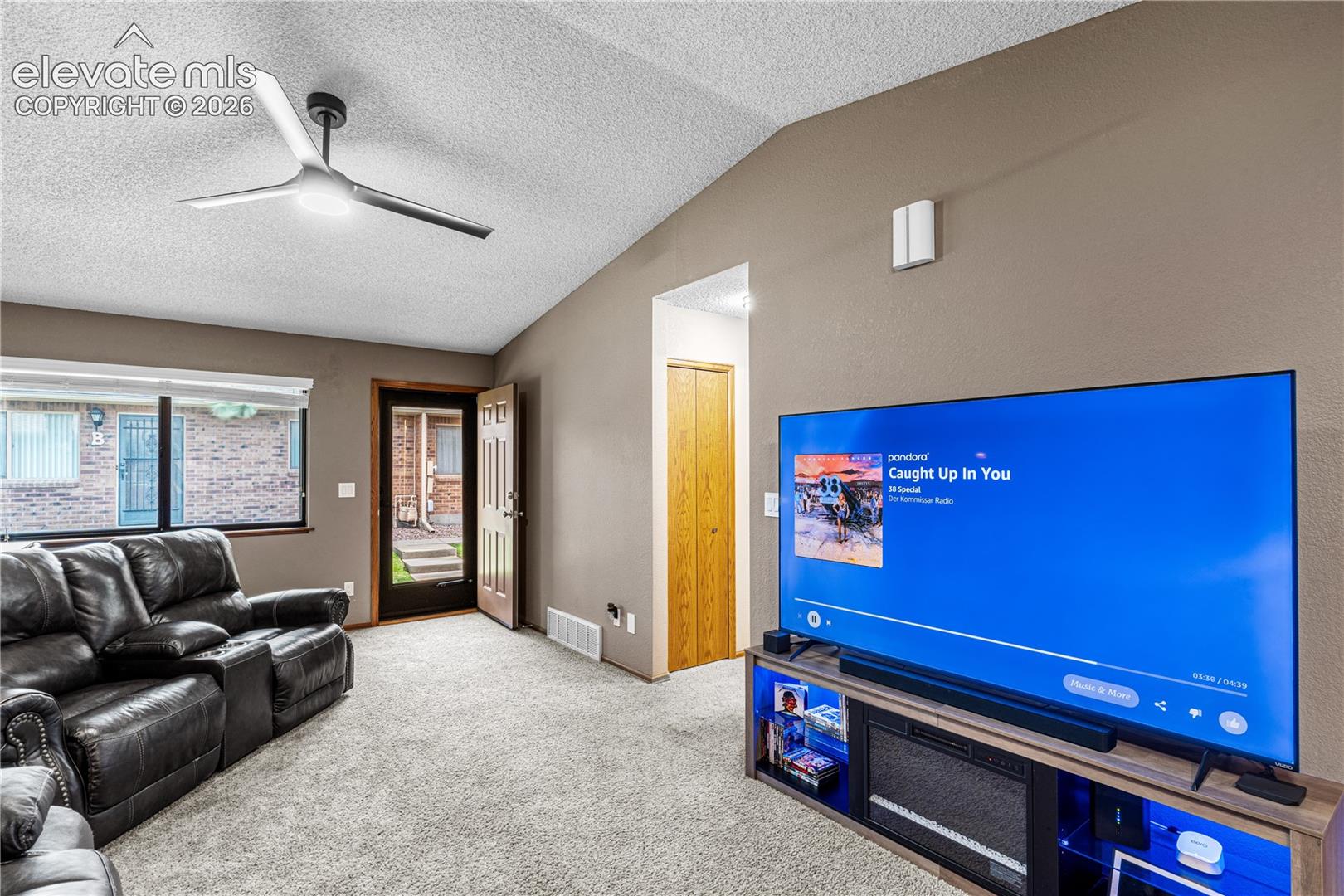 Vaulted ceilings featuring a modern three-blade ceiling fan, neutral wall-to-wall carpeting, and a window providing natural light