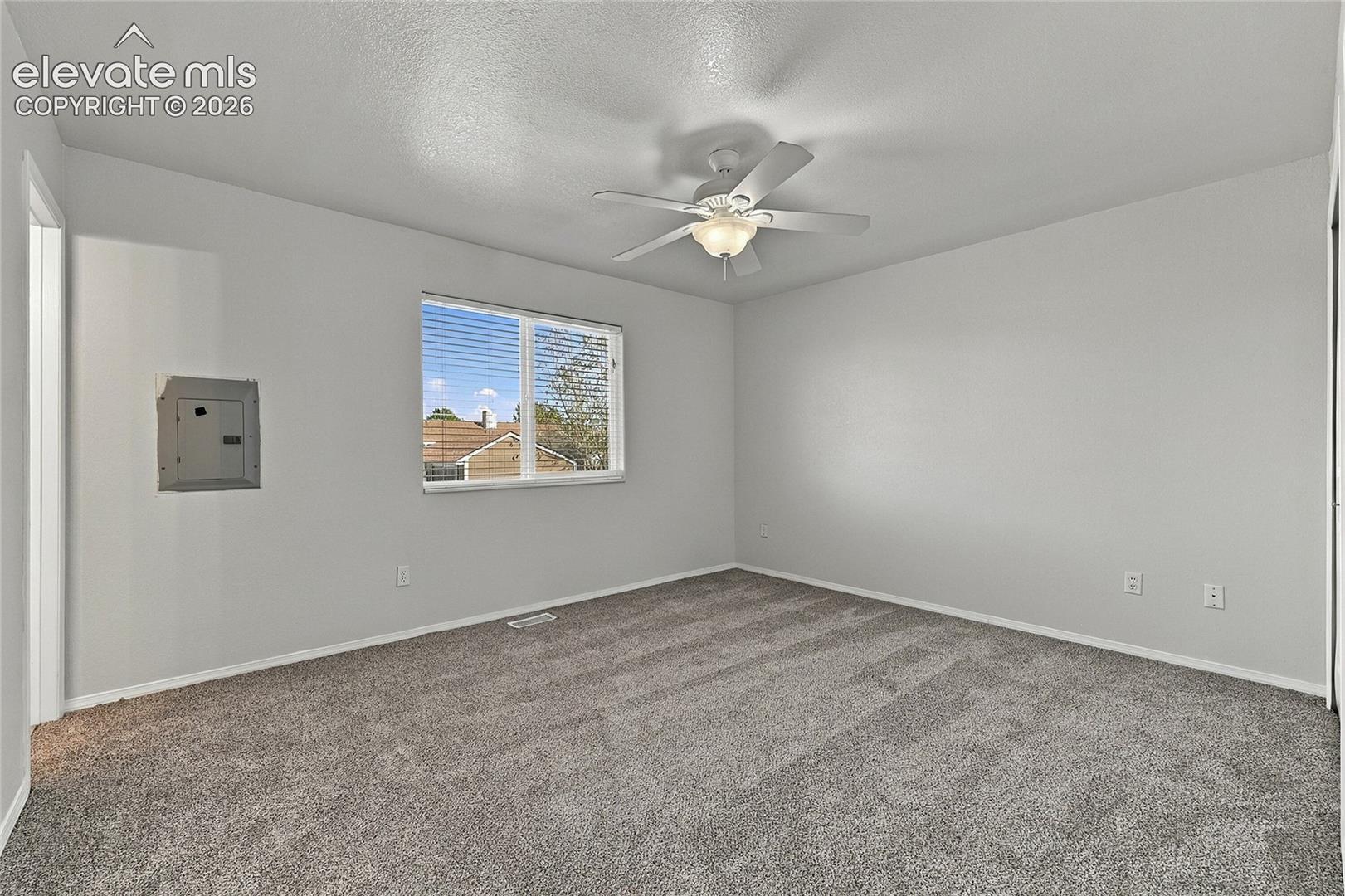 Neutral-toned carpeting, white walls, ceiling fan with integrated lighting, and a single-pane window