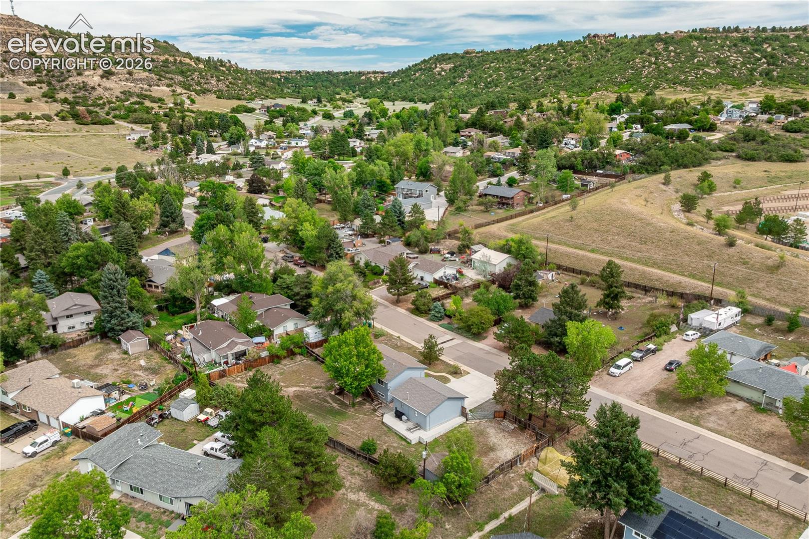 Aerial perspective of a suburban neighborhood featuring mature deciduous trees, expansive landscape topography, and rolling foothills