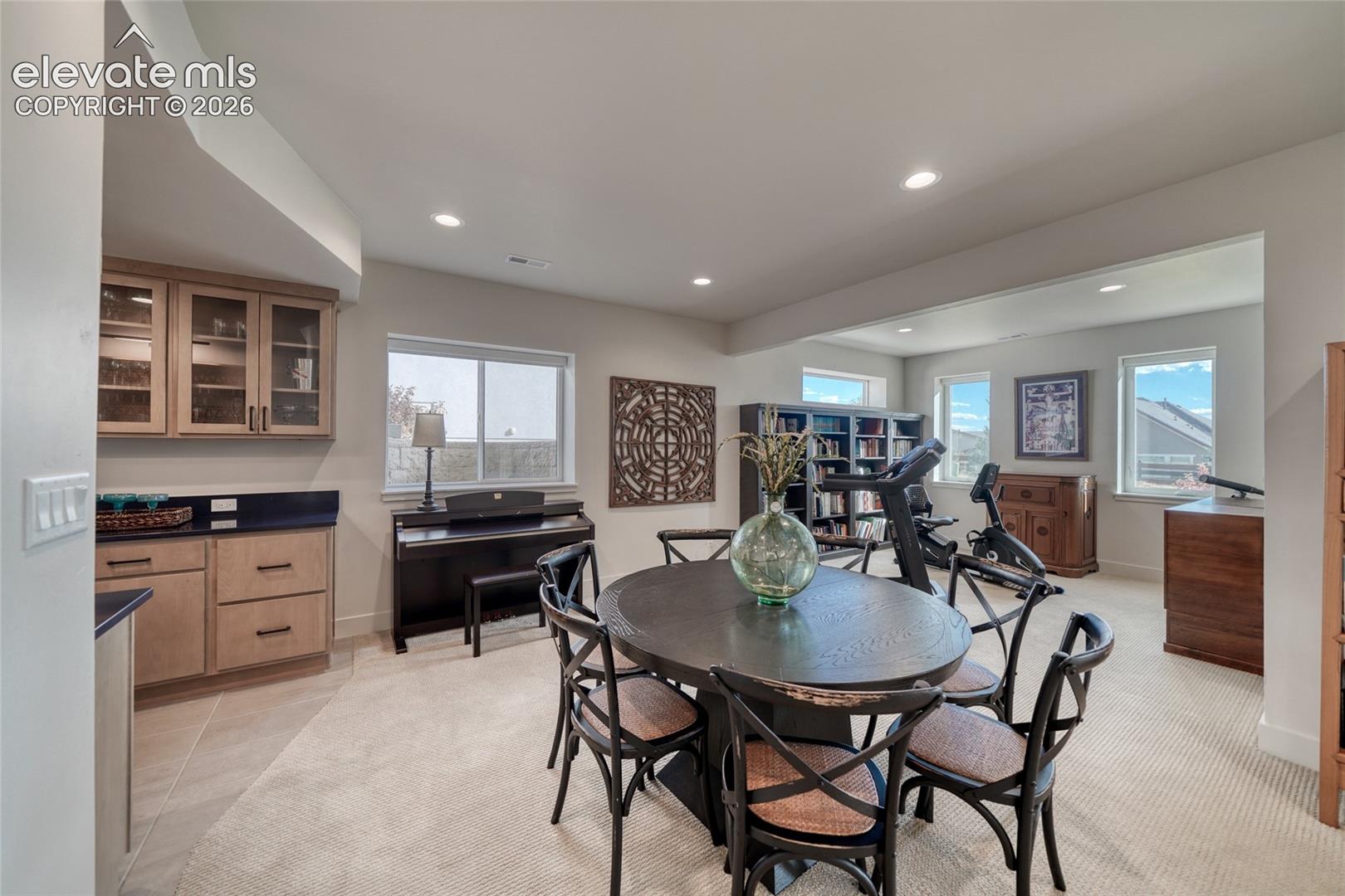 Open-concept space featuring custom built-in cabinetry with glass-front uppers and stone countertops, recessed lighting, and multiple windows providing natural light