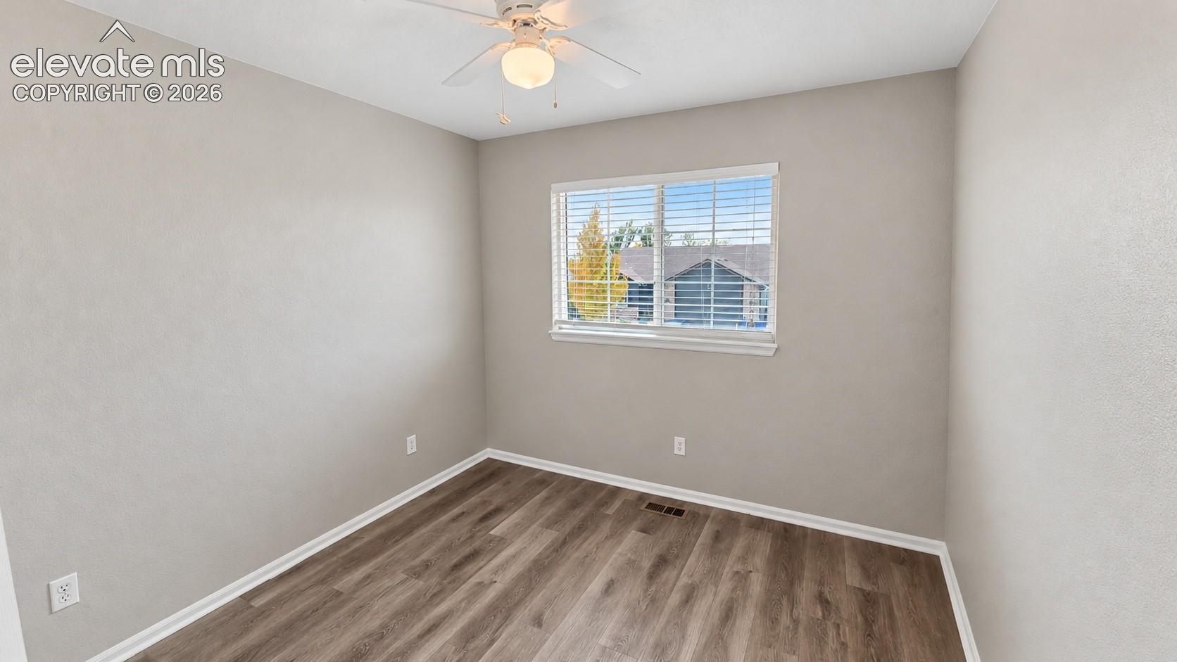 Neutral-toned interior room featuring wood-finish flooring, a ceiling-mounted light fixture with fan, and a single-pane window with horizontal blinds