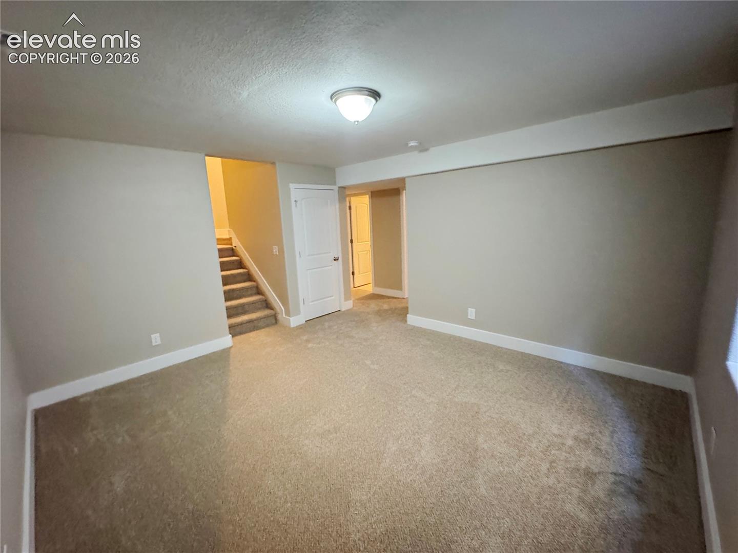 Neutral-toned interior space featuring wall-to-wall carpeting, flush-mount lighting, and solid-core interior doors