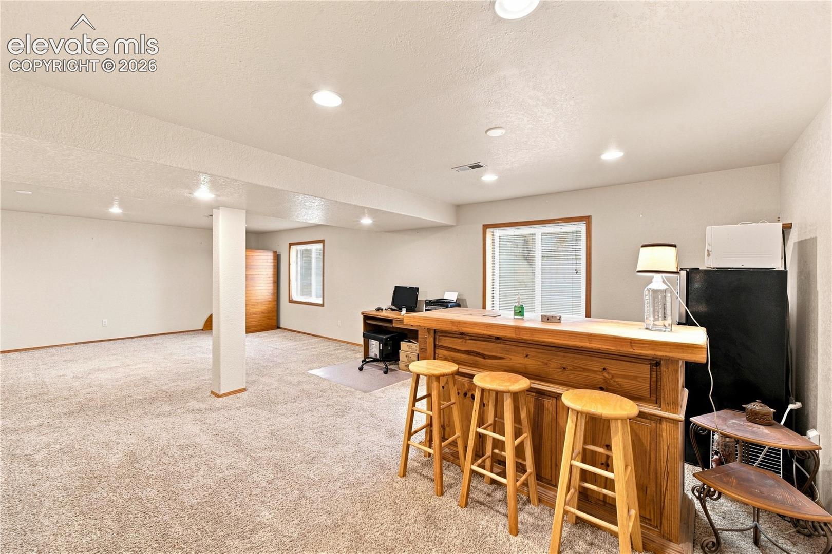 Open lower level featuring recessed lighting, a wooden built-in bar, and neutral carpeting