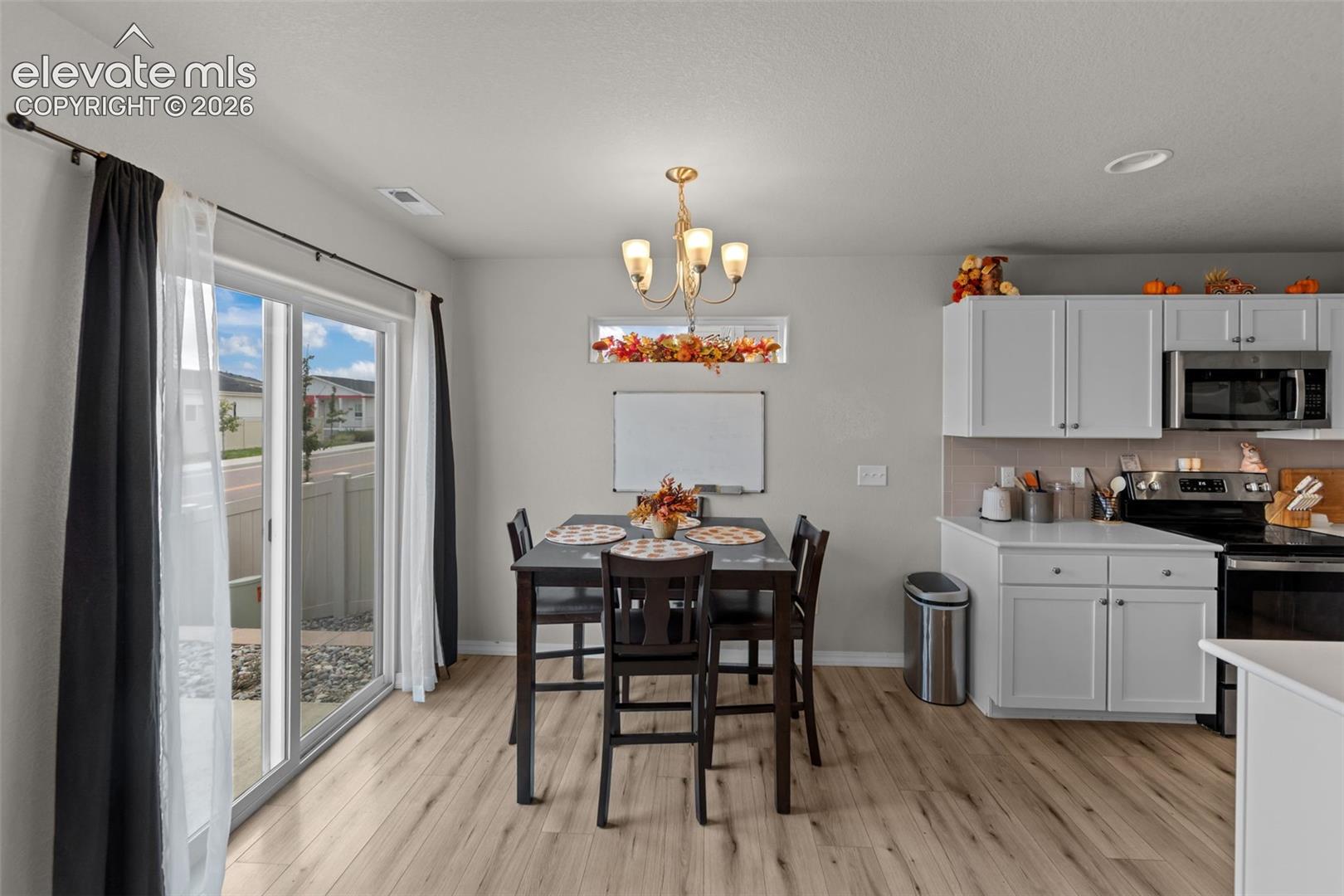 Light wood-finish flooring throughout, a glass sliding door, and white upper and lower cabinetry with stainless steel appliances