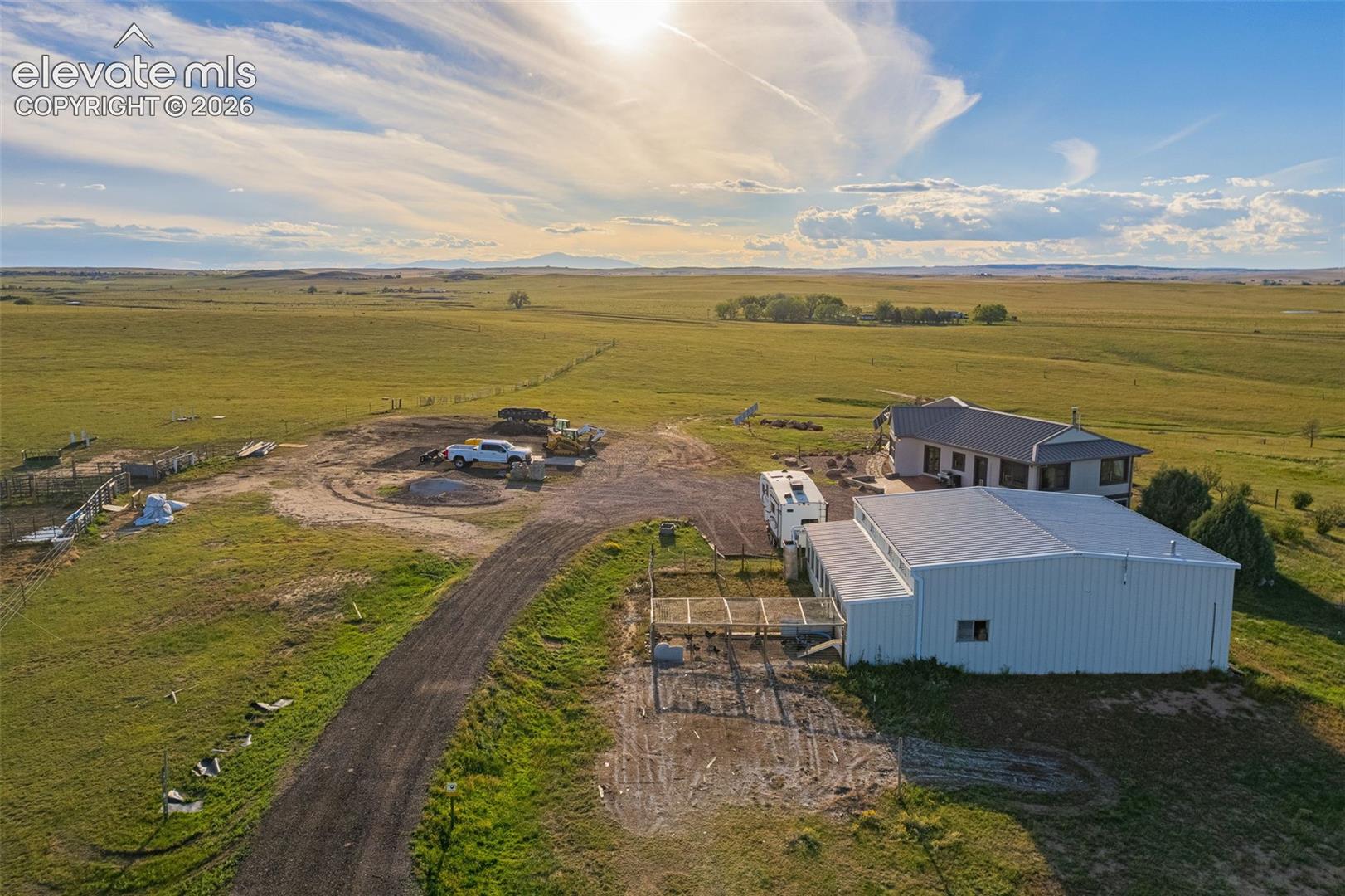 Extensive open land with a gravel driveway, a modern metal outbuilding, and a single-story residence