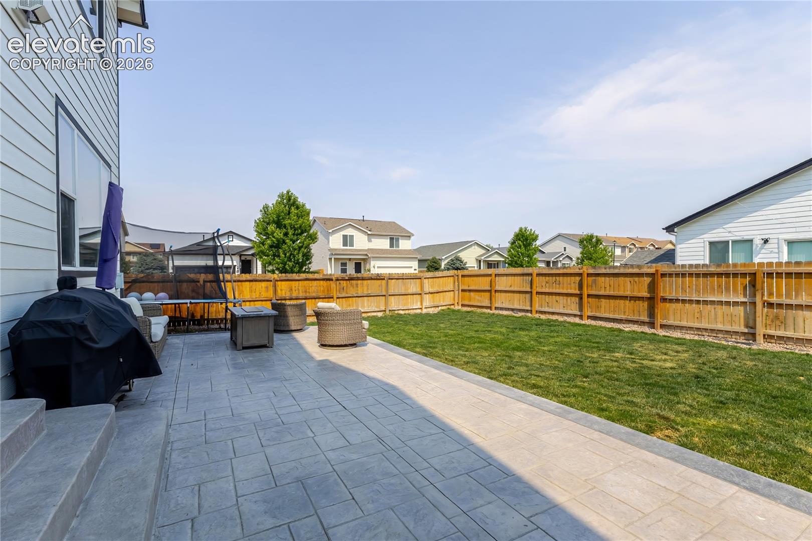 Expansive backyard featuring a stamped concrete patio, a manicured lawn, a wooden privacy fence, and vinyl siding