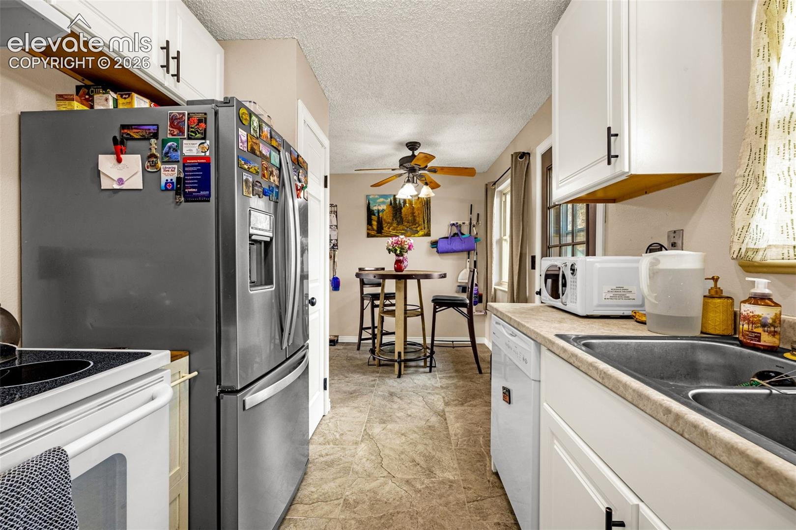 Kitchen featuring white cabinetry with matte black hardware, stainless steel refrigerator, neutral-toned tile flooring, and ceiling fan with light fixture