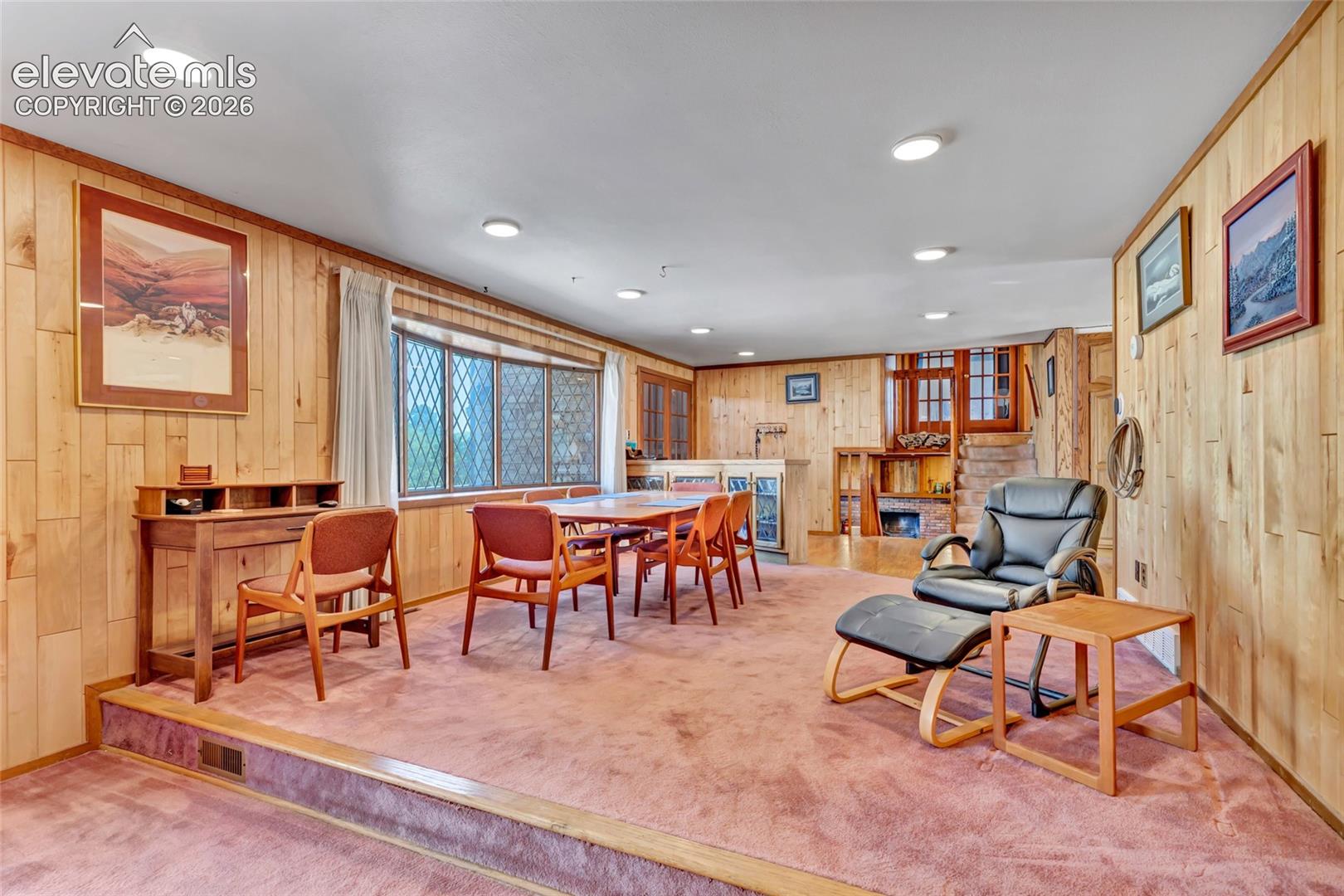 Recessed lighting illuminates the wood-paneled walls and a raised platform with a dining area