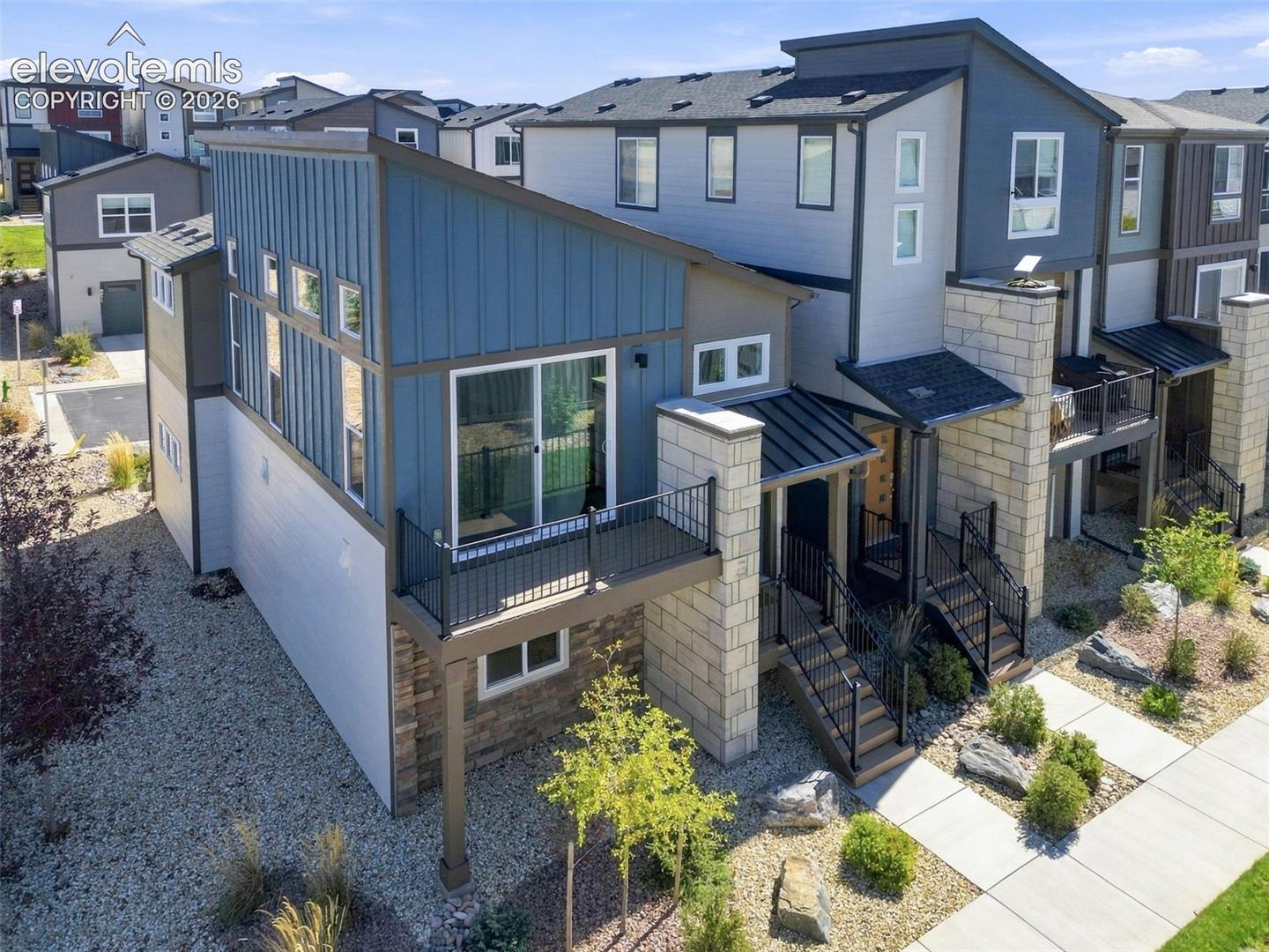 Modern multi-level exterior featuring vertical metal siding, stacked stone masonry, a raised balcony with metal railings, and a metal-clad shed roofline