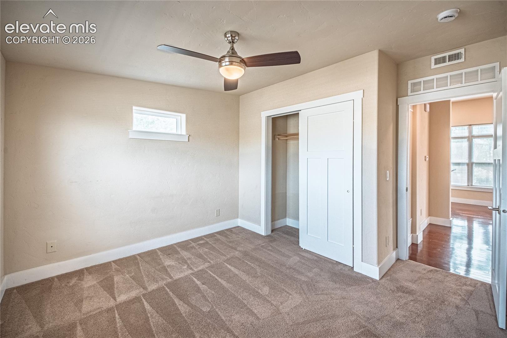 Carpeted room featuring a ceiling fan with integrated lighting, a horizontal window, and a built-in closet with sliding white paneled doors