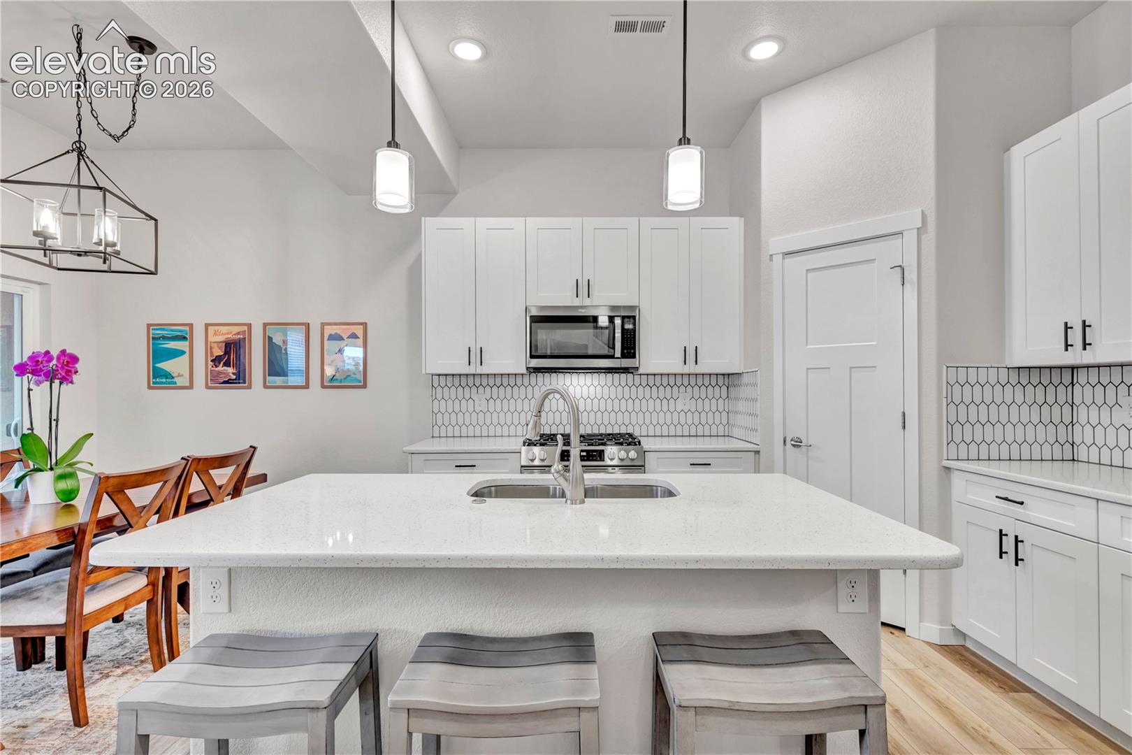 Contemporary kitchen featuring a large central island with an undermount sink, white cabinetry, integrated stainless steel appliances, and a geometric tile backsplash