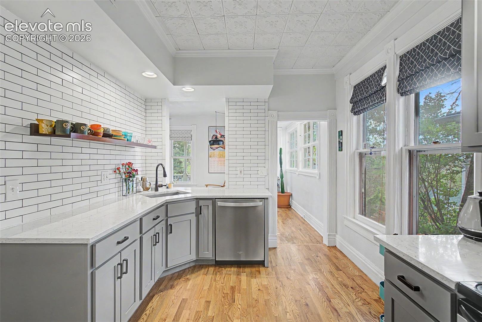Updated kitchen with light gray cabinetry, Victorian-style ceiling tile, white tile backsplash, white stone countertops, and hardwood flooring.