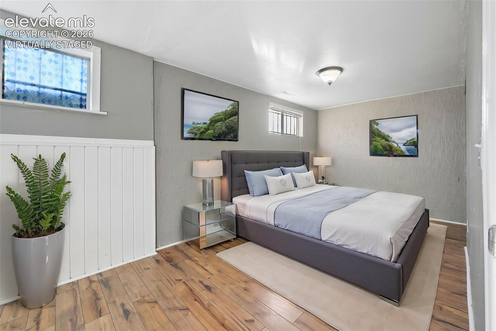 Virtually staged bedroom in the basement that is so large/long that it could be an office!    Neutral-toned room featuring LVP flooring, white vertical wainscoting, textured wall surfaces, and two recessed windows