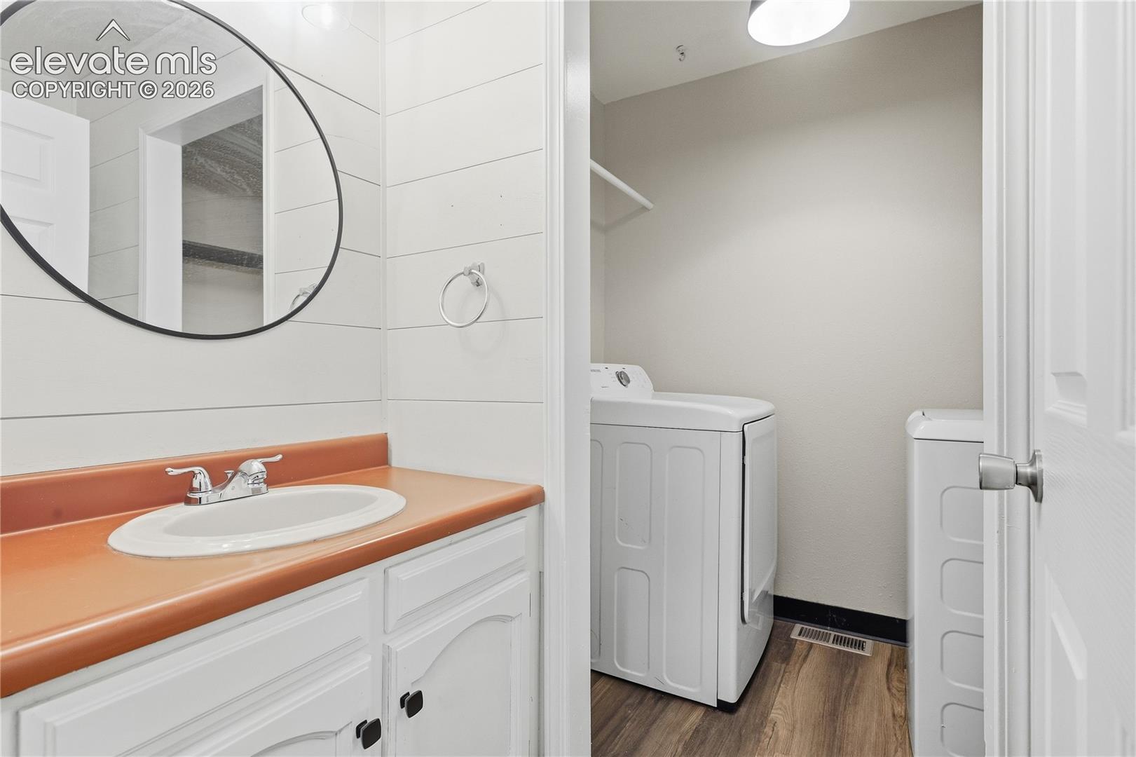 White vanity with dark hardware, a orange countertop, and a circular mirror
