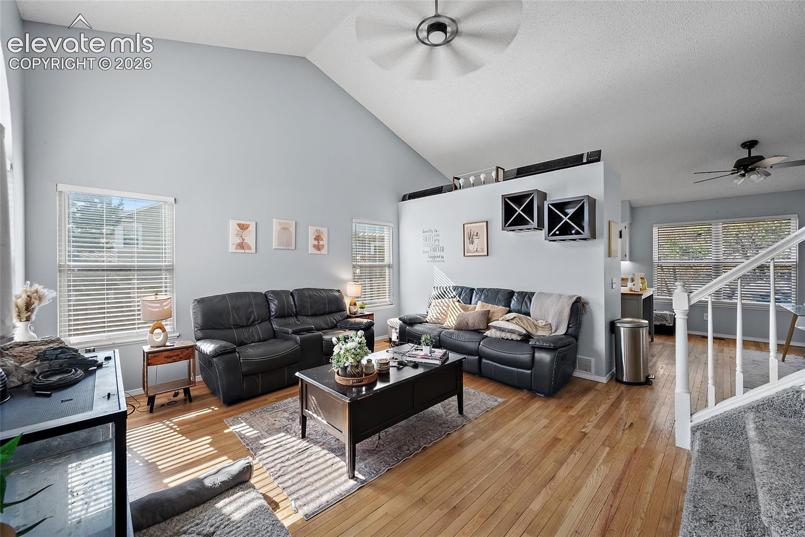 Vaulted ceiling, wood-finish flooring, multiple windows, ceiling fan, and built-in shelving