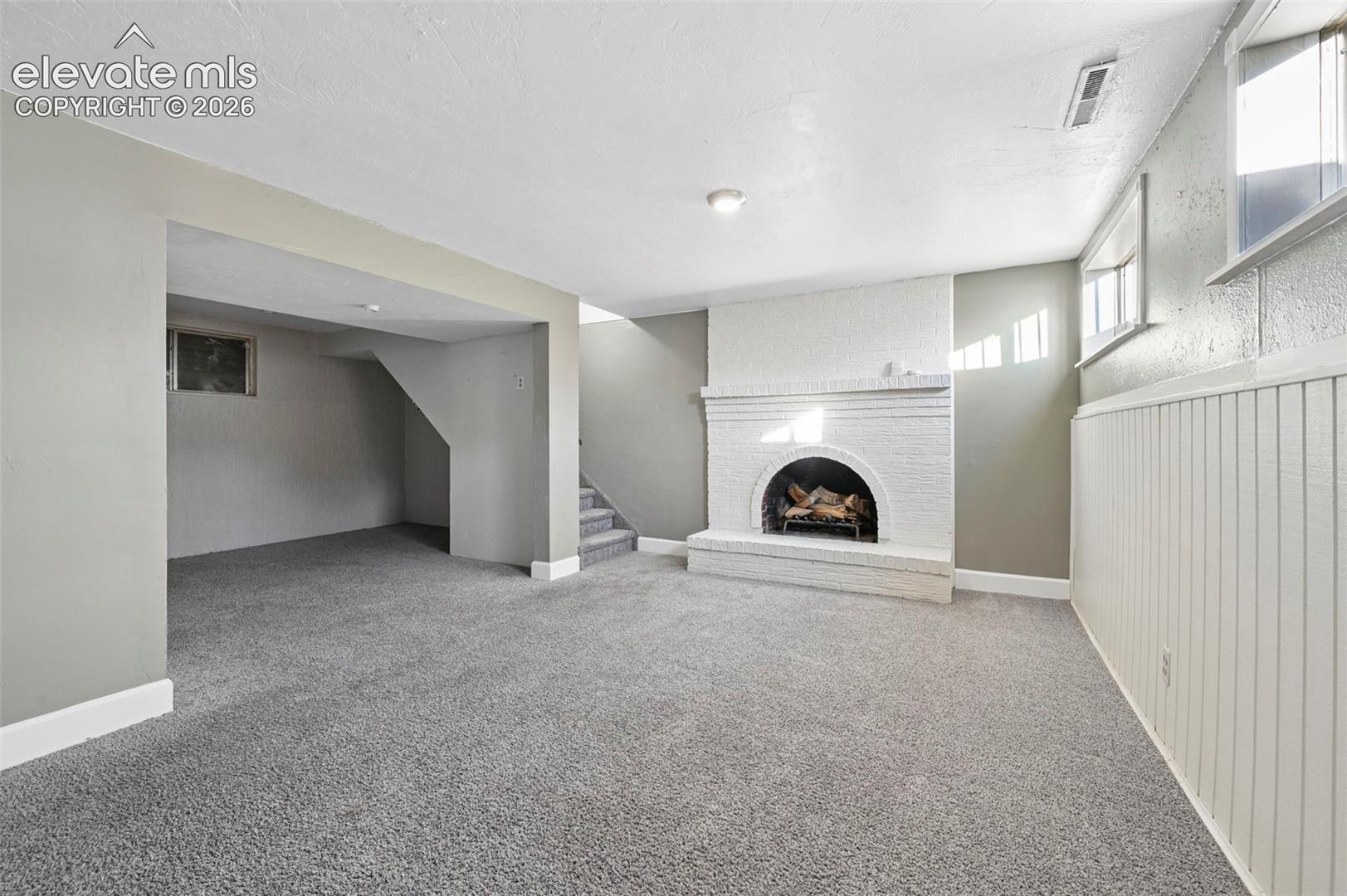 Finished interior space featuring neutral wall-to-neutral wall carpeting, a painted brick fireplace with an arched hearth, and vertical beadboard paneling