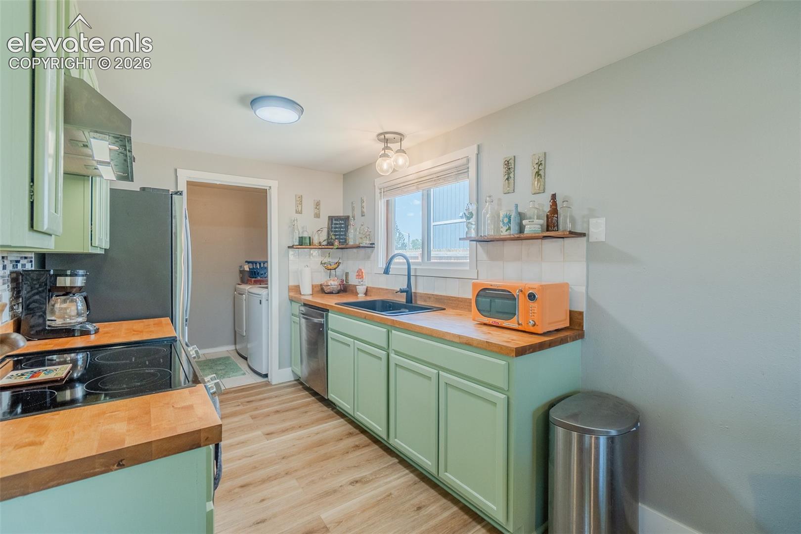 Kitchen featuring light green cabinetry, wood-finish countertops, and stainless steel appliances