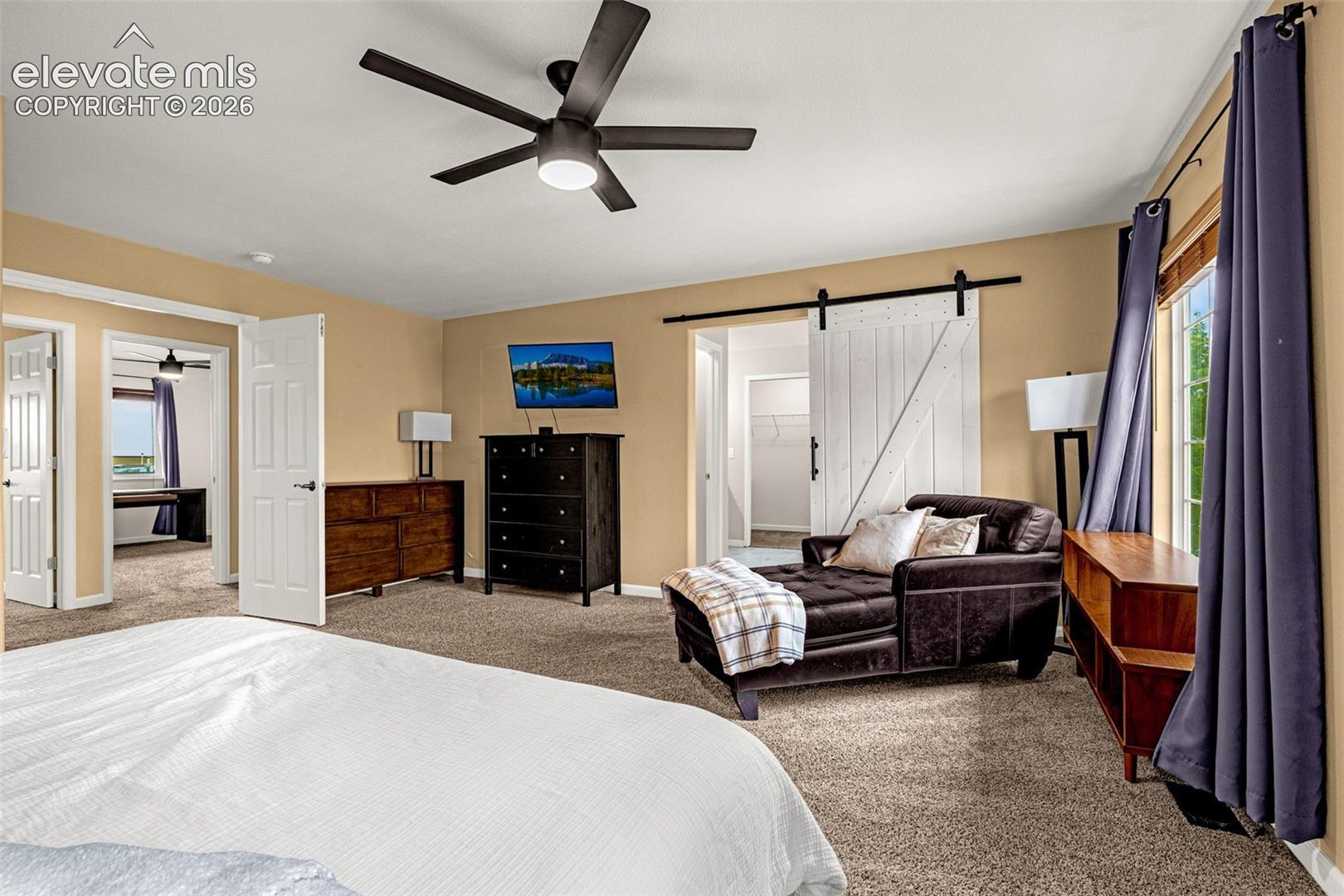 Spacious room featuring carpeting, a white sliding barn door, and a modern ceiling fan with integrated lighting