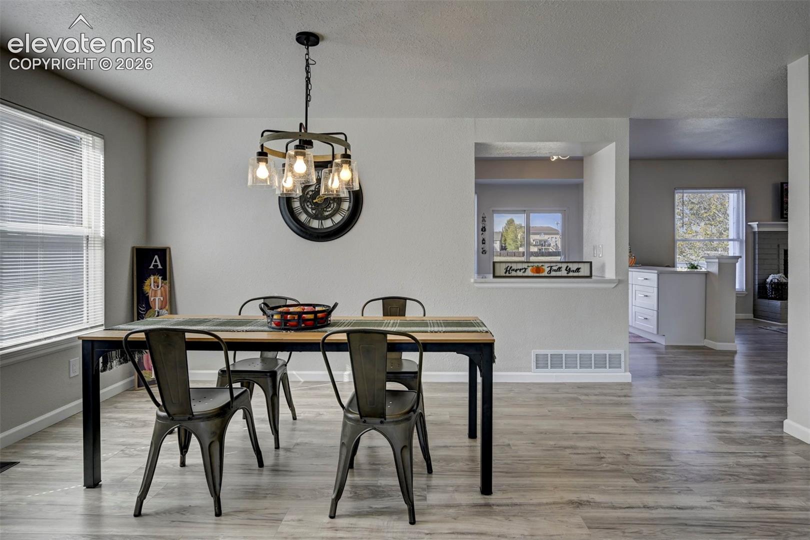 Dining space featuring wood-finish flooring, a multi-light industrial chandelier, and a cut-out wall pass-through