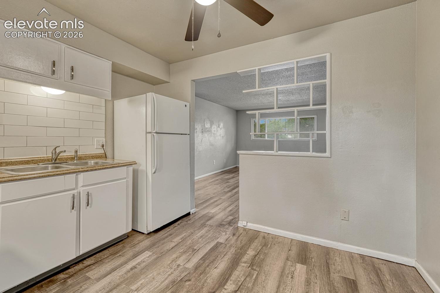 Bright kitchen featuring white cabinetry, subway tile backsplash, stainless steel refrigerator, and wood-finish flooring