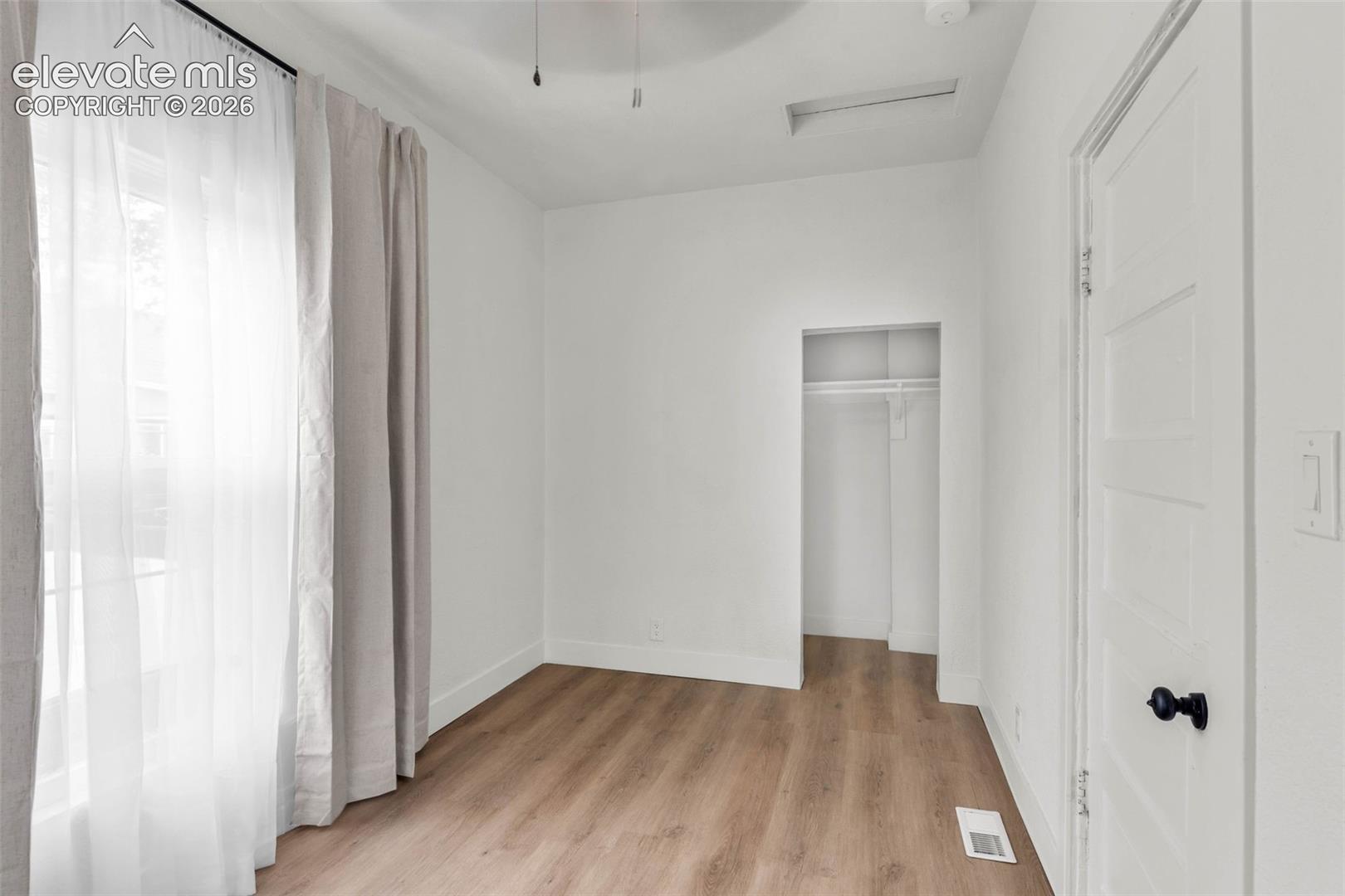 Interior room featuring wood-finish flooring, a reach-in closet with integrated shelving, and a ceiling fan with light fixture