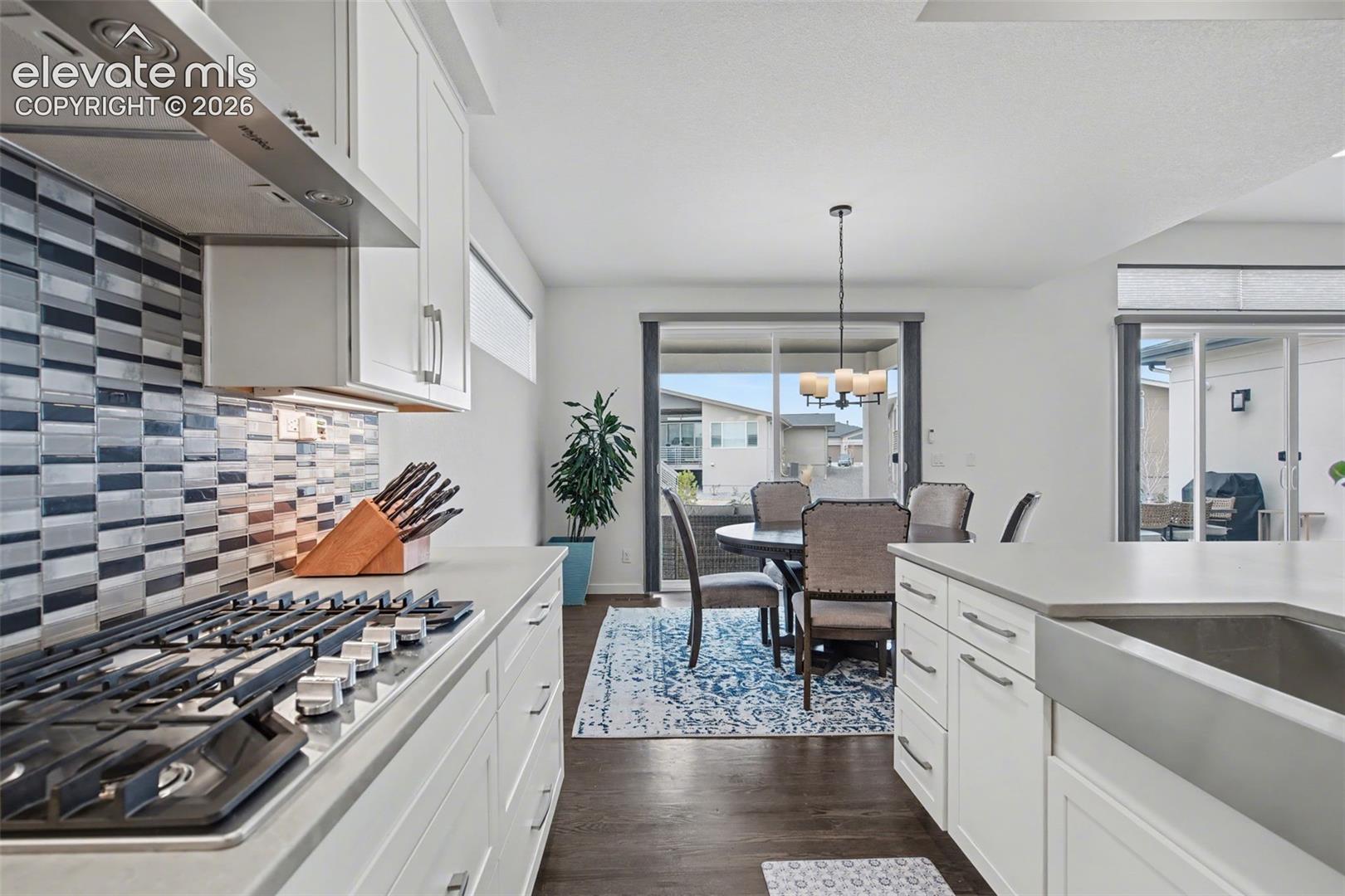 Kitchen featuring white cabinets, stainless steel gas cooktop, suspended lighting, dark wood finished floors, and backsplash