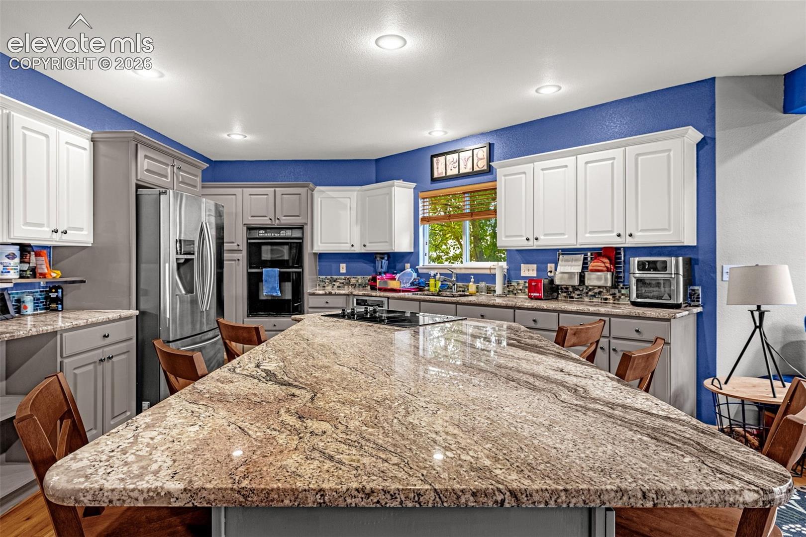 Spacious kitchen featuring a large island with a stone surface, recessed lighting, and built-in stainless steel appliances