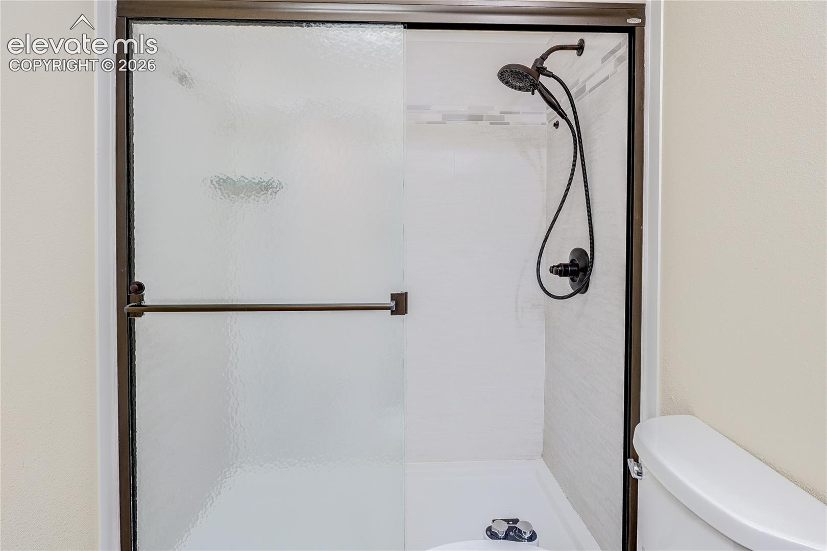 Walk-in shower featuring a dark-finish frame, textured glass sliding door, integrated shower head with handheld attachment, and horizontal tile accent inlay