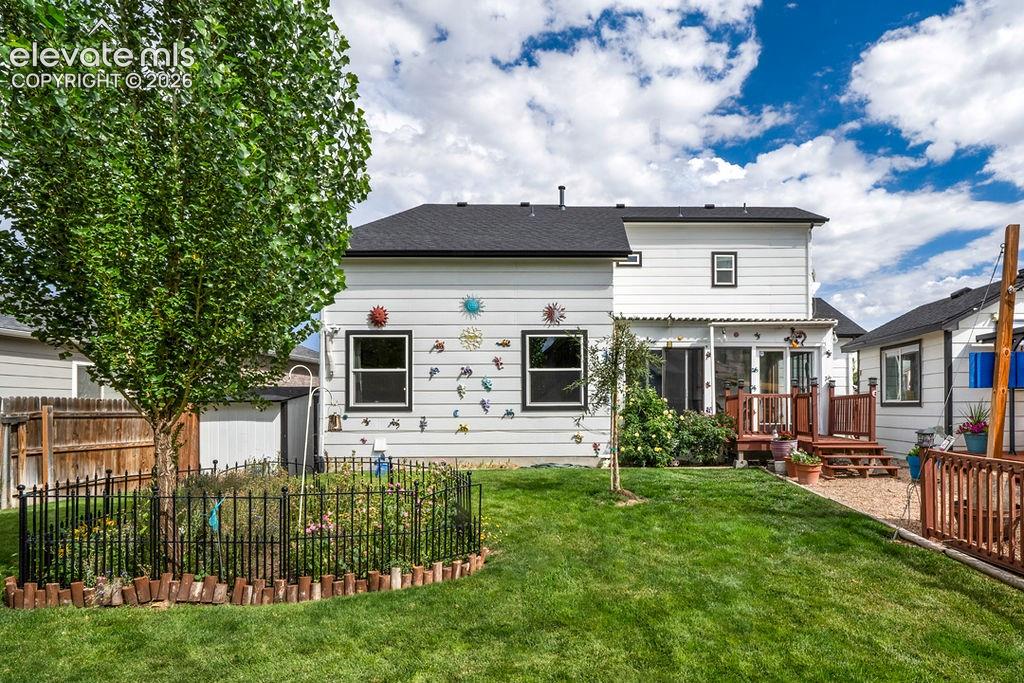 Expansive backyard featuring a green lawn, established tree, and a garden bed with wrought iron fencing