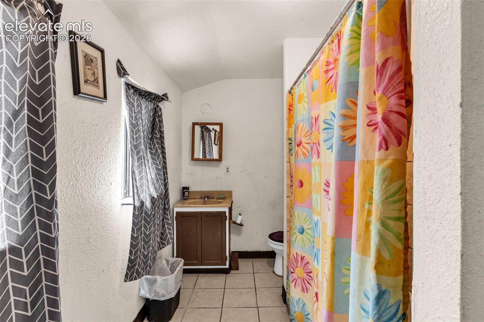 Bathroom featuring a single-sink vanity with wood-finish cabinetry, tile flooring, and a window