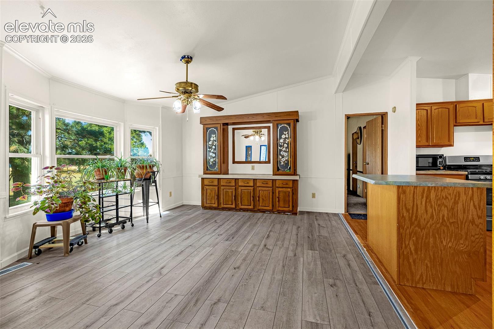 Wood-finish flooring, vaulted ceiling with a central fan, large multi-pane windows, and a custom built-in wood hutch with glass-panel accents