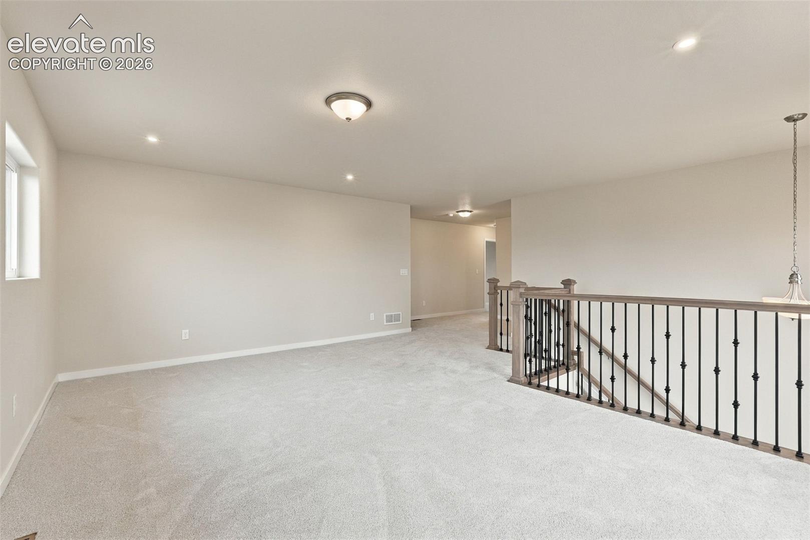 Open-concept area featuring wall-to-wall carpeting, recessed lighting, and a decorative staircase railing with iron spindles and a stained wood-finish banister