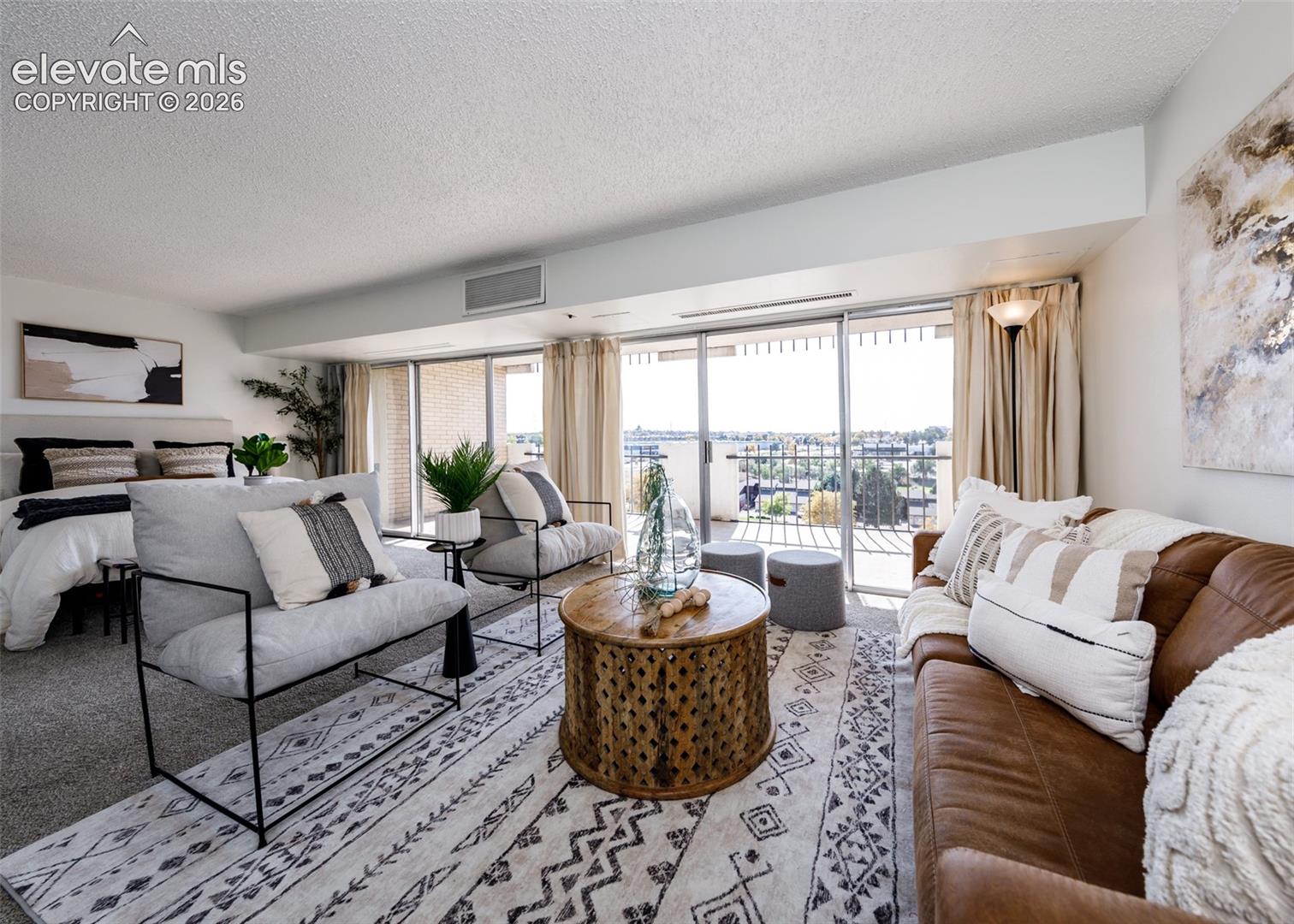 Floor-to-ceiling sliding glass doors, private balcony with metal railing, and neutral wall-to-wall carpeting