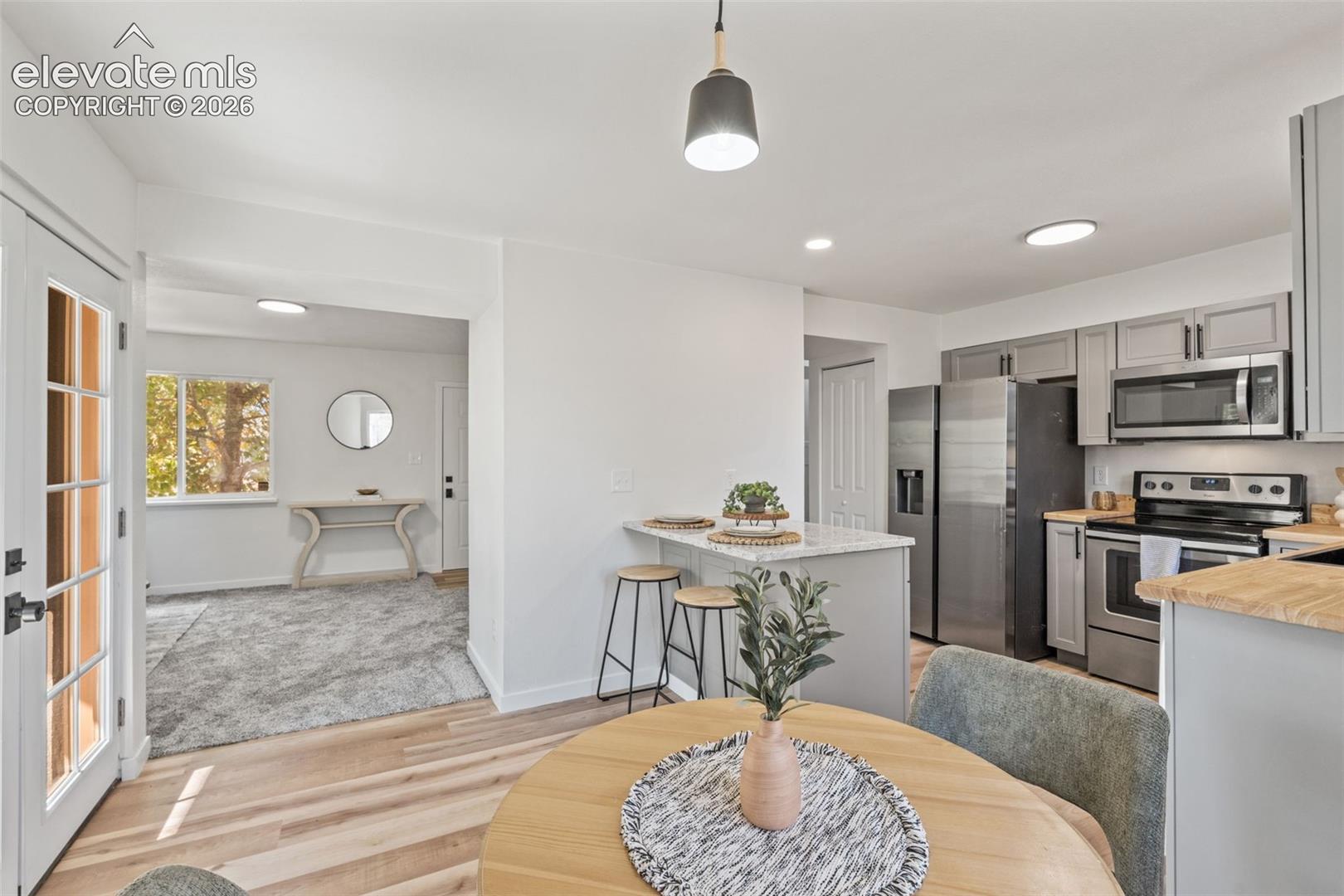 Kitchen featuring light gray cabinetry, stainless steel appliances, a stone-surface breakfast bar, and wood-finish flooring