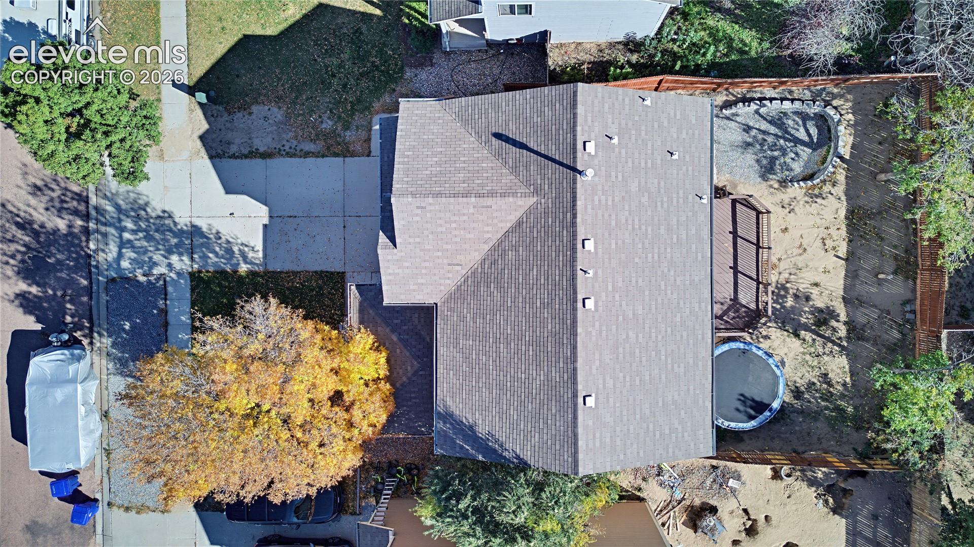 Aerial view featuring a multi-gabled asphalt shingle roof, concrete driveway, and enclosed backyard with wooden fencing