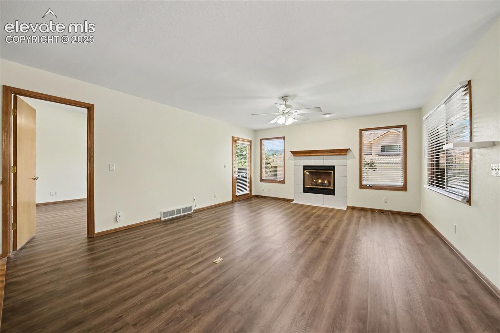 New LVP flooring throughout, white-tiled fireplace with wood mantel, ceiling fan, and multiple windows providing natural light
