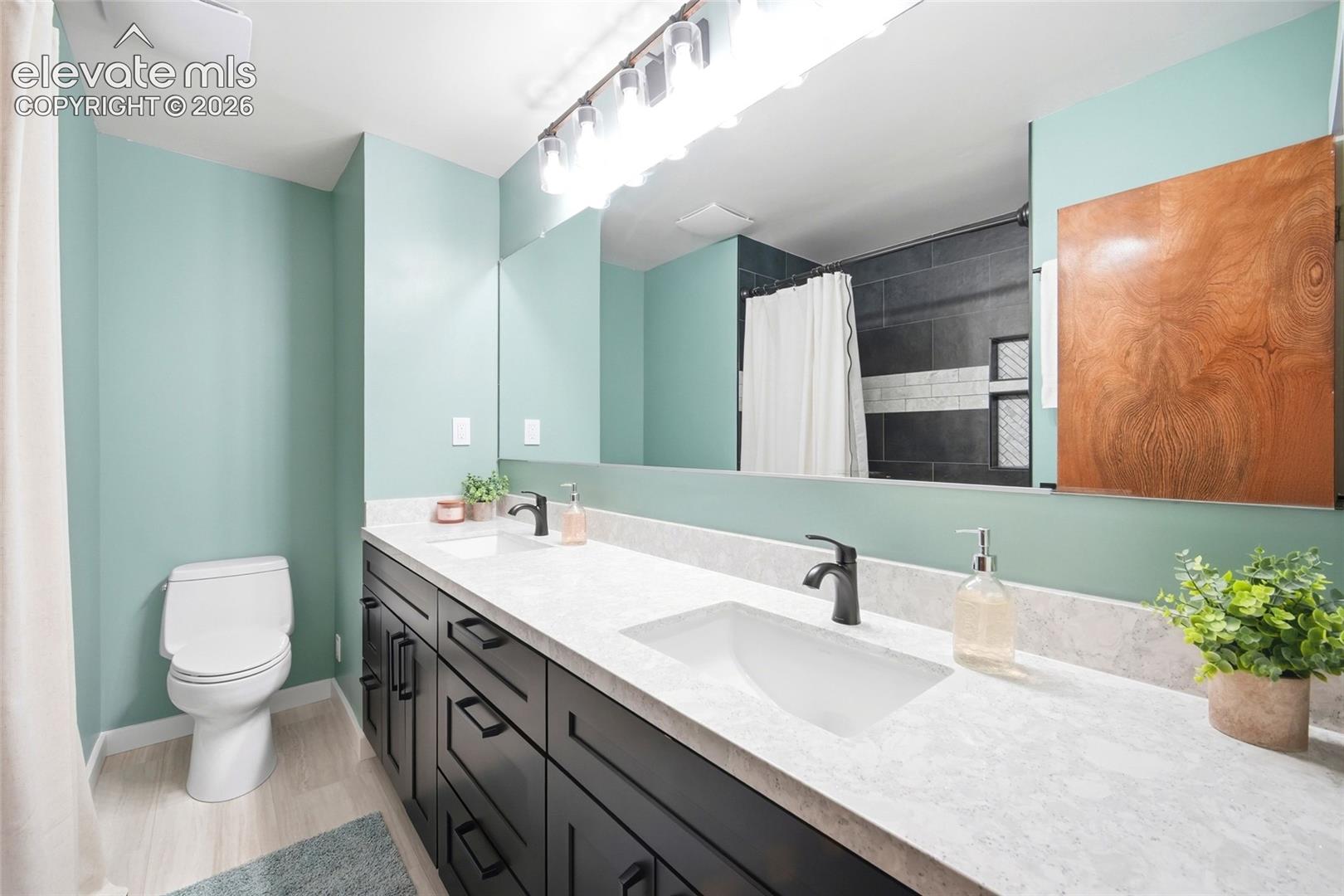 Double vanity featuring dark cabinetry, stone-finish countertops, undermount sinks, matte black fixtures, and a full-width mirror