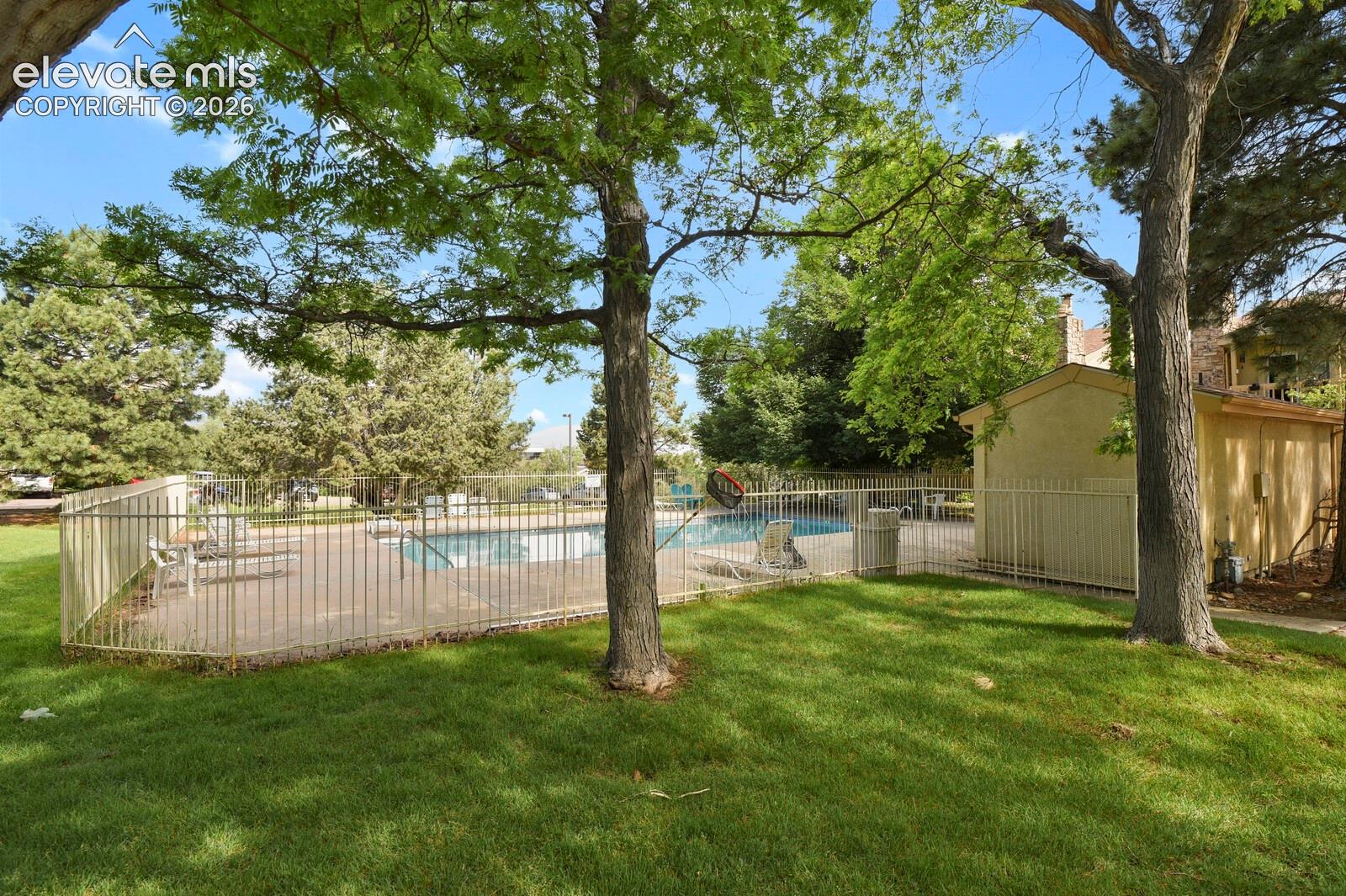 In-ground swimming pool enclosed by metal fencing, surrounded by a grass lawn and mature trees, shown here in the summer.  The pool is now winterized