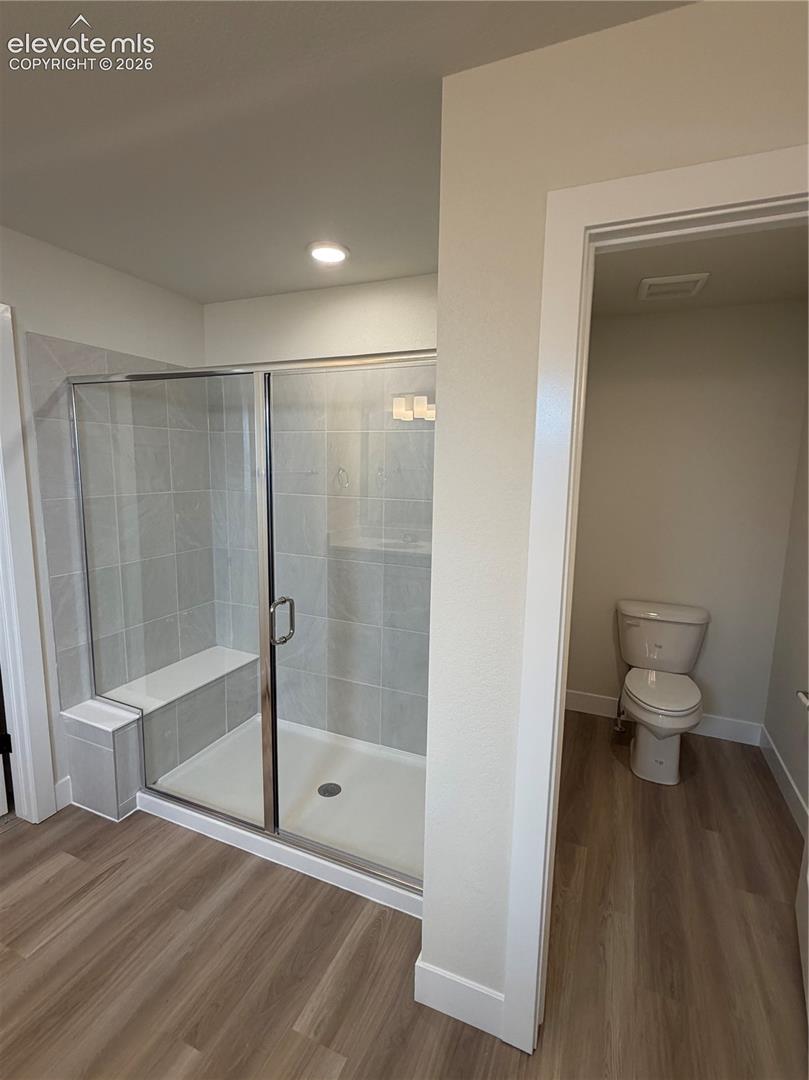 Walk-in shower featuring a built-in bench, glass enclosure, and light-toned tile surround, wood-finish flooring, and a separate water closet area