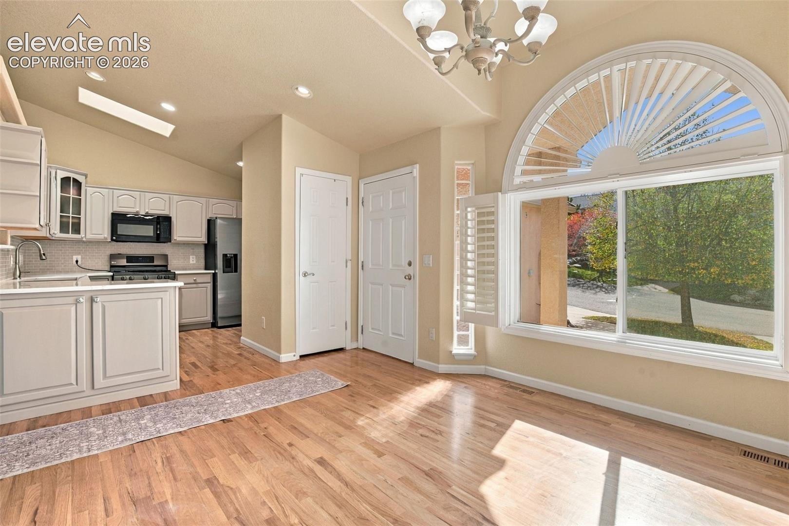Vaulted ceiling, wood-finish flooring, custom shaker-style cabinetry, and large arched window with integrated shutters
