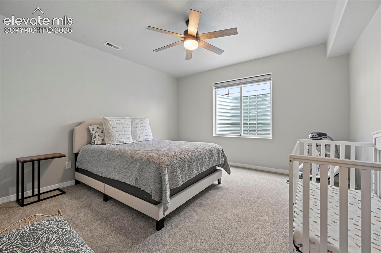 Neutral-toned interior featuring wall-to-wall carpeting, a multi-blade ceiling fan with integrated lighting, and a single-hung window with a corrugated metal egress well