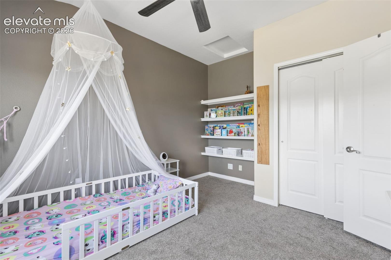 Ceiling fan, wall-mounted shelving, built-in closet with sliding doors, neutral carpeting, and a skylight
