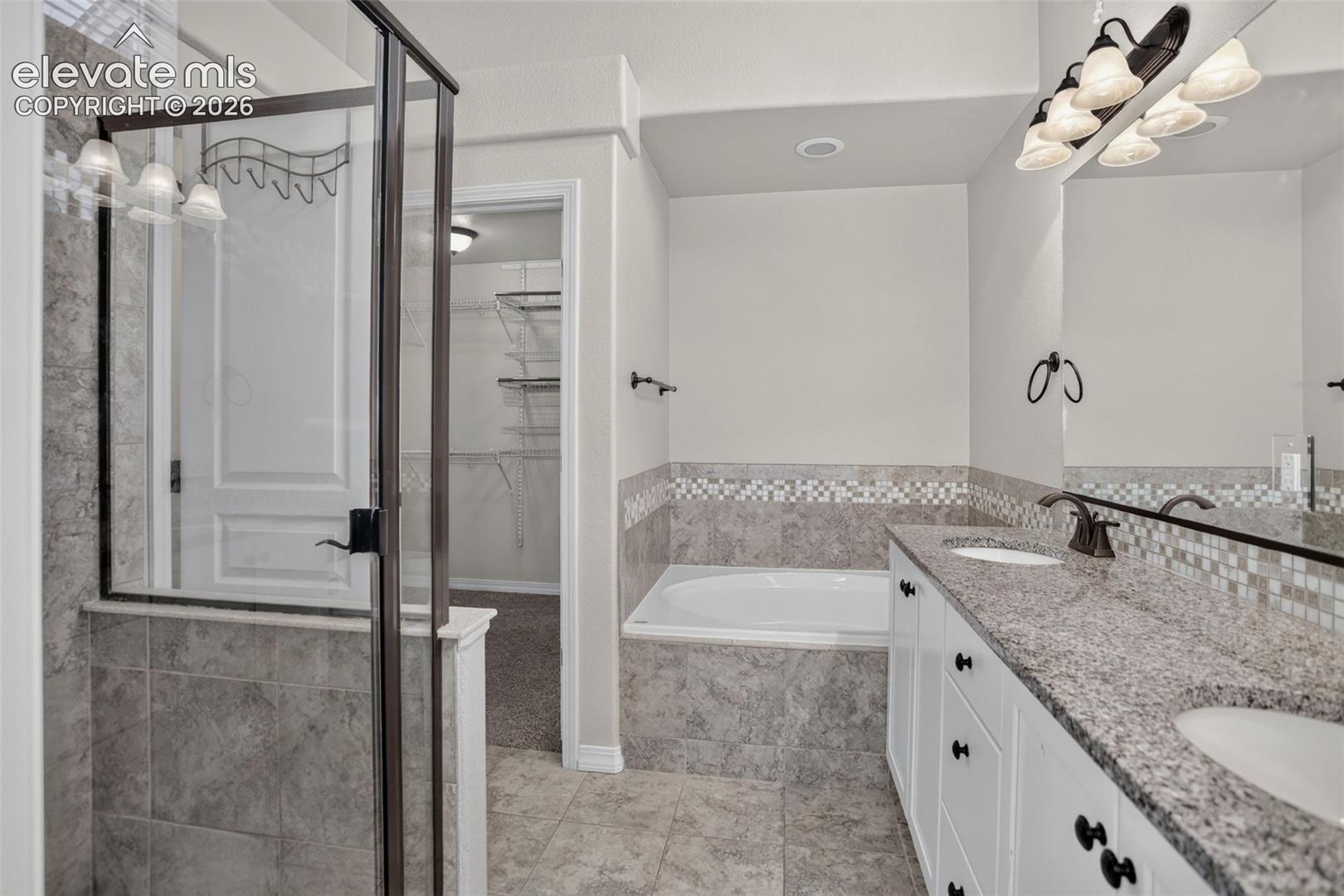 Double vanity with integrated sinks, granite countertop, tile flooring, glass-enclosed shower, and built-in soaking tub