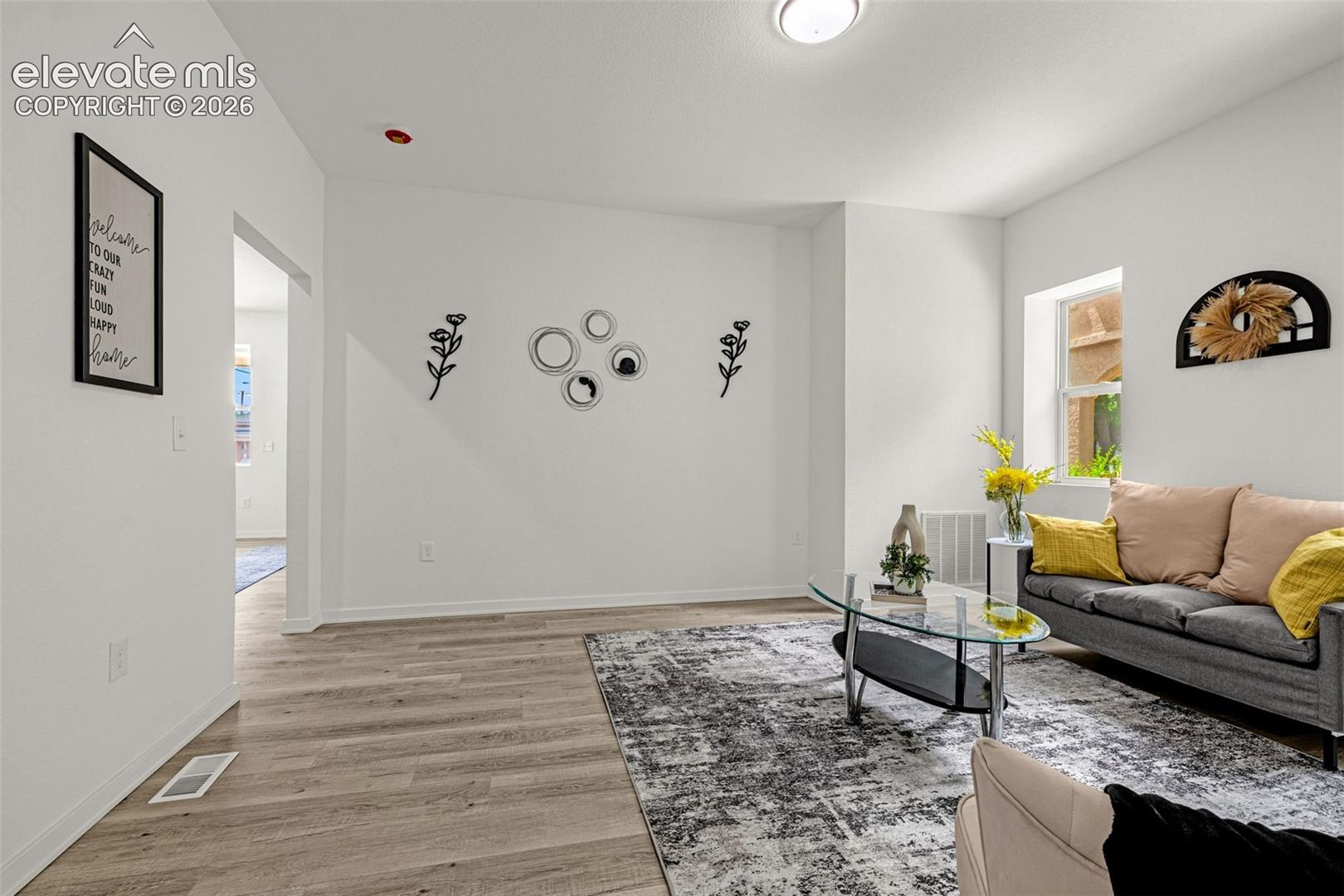 Bright living area featuring wood-finish flooring, white walls, and a visible window