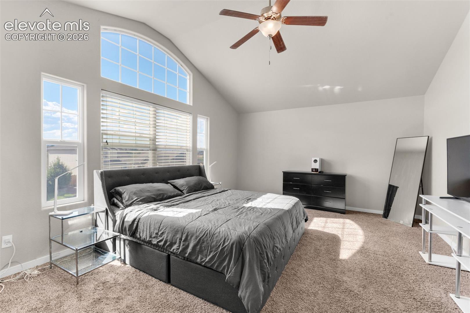 Vaulted ceiling with a central multi-blade ceiling fan, expansive arched window, and additional rectangular windows