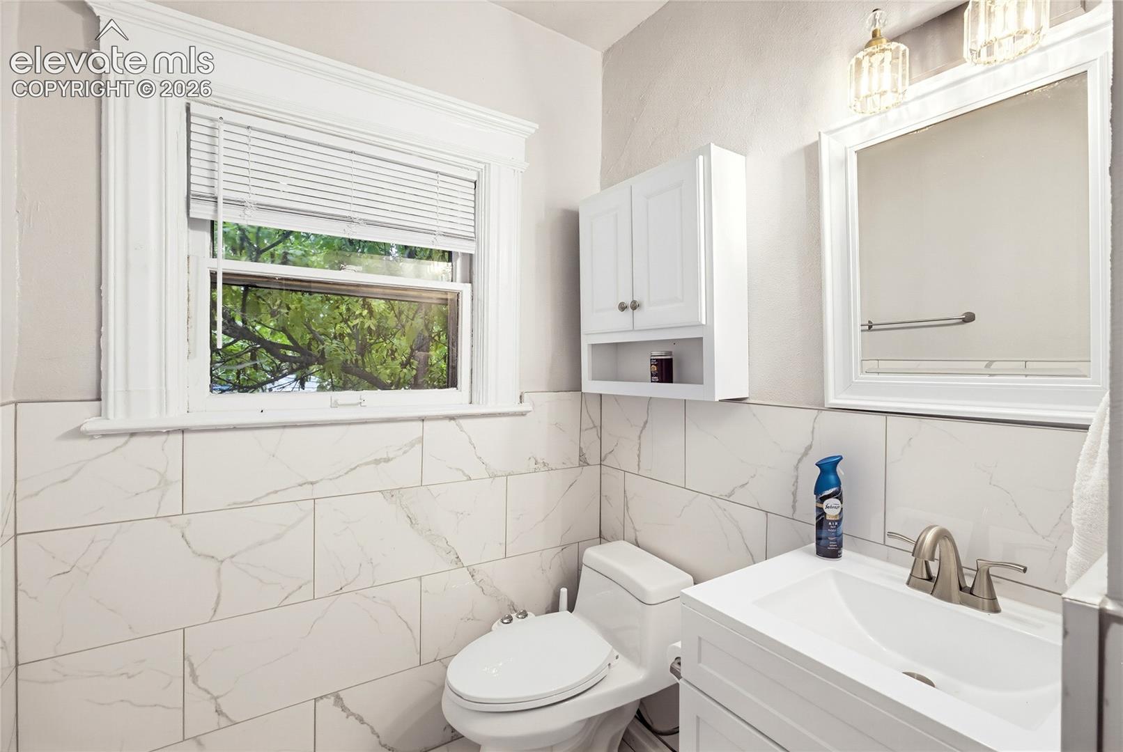 White subway tile with gray veining, white framed window, wall-mounted cabinet, vanity with integrated sink, and brushed nickel faucet