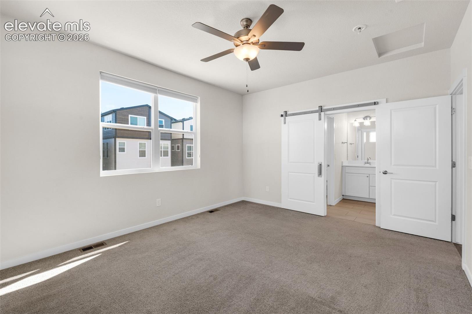 Neutral-toned bedroom featuring carpeted flooring, a ceiling fan with integrated lighting, a sliding door on a metal track, and large windows