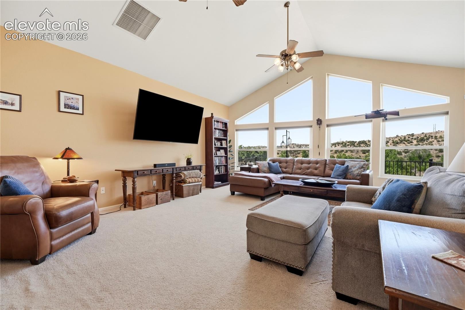 Vaulted ceiling, expansive windows, ceiling fan, and carpeted flooring