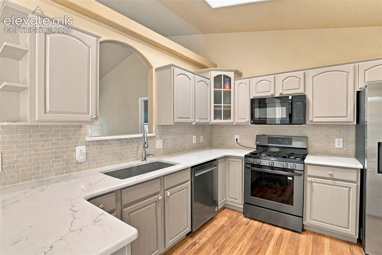 Kitchen featuring light cabinetry, subway-tiled backsplash, neutral-toned stone-finish countertops, stainless steel appliances, and wood-finish flooring