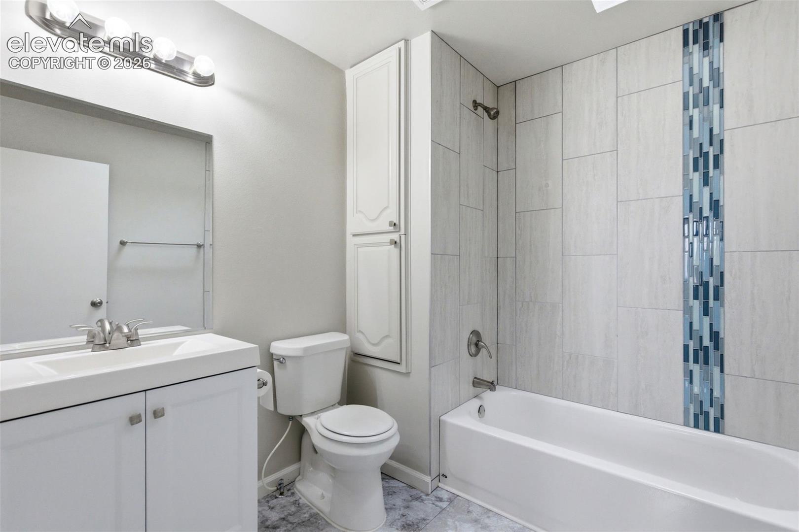Bathroom featuring a tiled tub shower with a decorative vertical tile accent, a white vanity with integrated sink, and white overhead storage cabinetry
